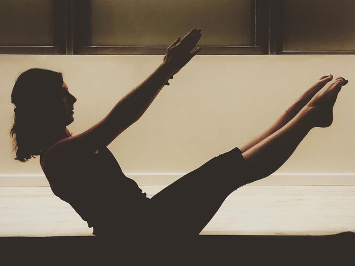 Silhouette en posture de pilates, jambes tendues et bras levés.
